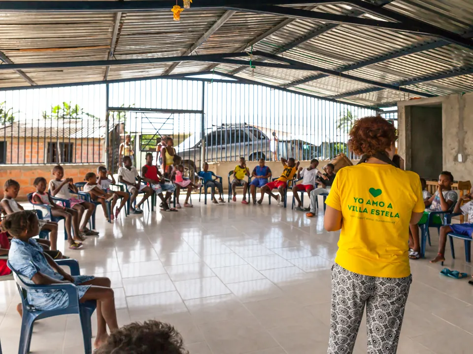 Encuentro comunitario con niños y adultos sentados en círculo en un salón abierto
