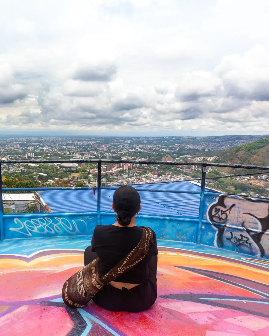Mujer sentada en un mirador pintado, contemplando la ciudad de Cali
